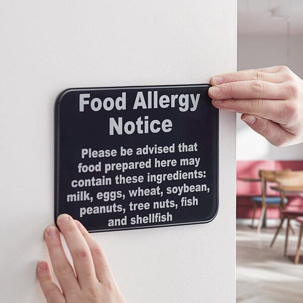 A person holding a black and white plastic "Food Allergy Notice" sign.