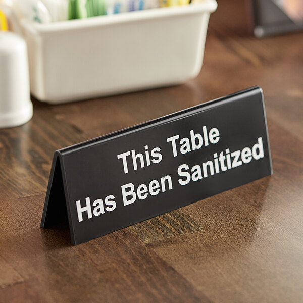 A black and white plastic sign that says "This table has been sanitized" on a table.