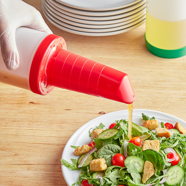 A hand in gloves using a red Tablecraft PourMaster spout to pour yellow liquid over a salad.