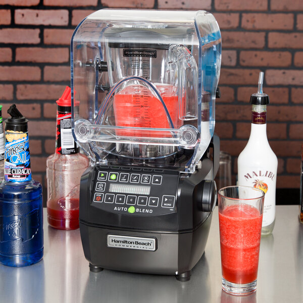A Hamilton Beach commercial bar blender on a counter with a glass of red liquid next to it.