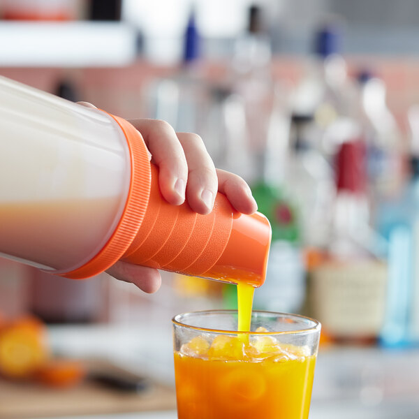 A hand using a Tablecraft PourMaster orange neck spout to pour orange liquid into a glass.