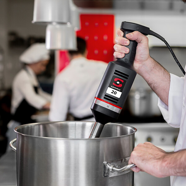 A man using a Sammic medium-duty immersion blender in a metal container.