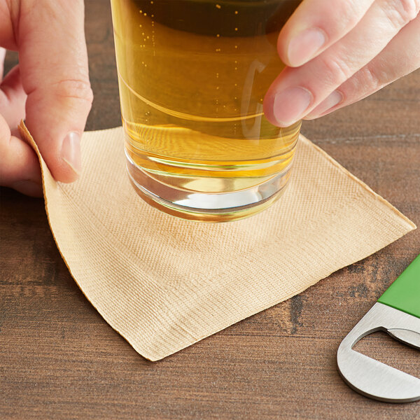 A hand holding an EcoChoice beverage napkin with a glass of beer.