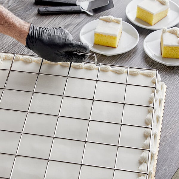 A person using a Choice stainless steel grid to cut a yellow and white sheet cake.