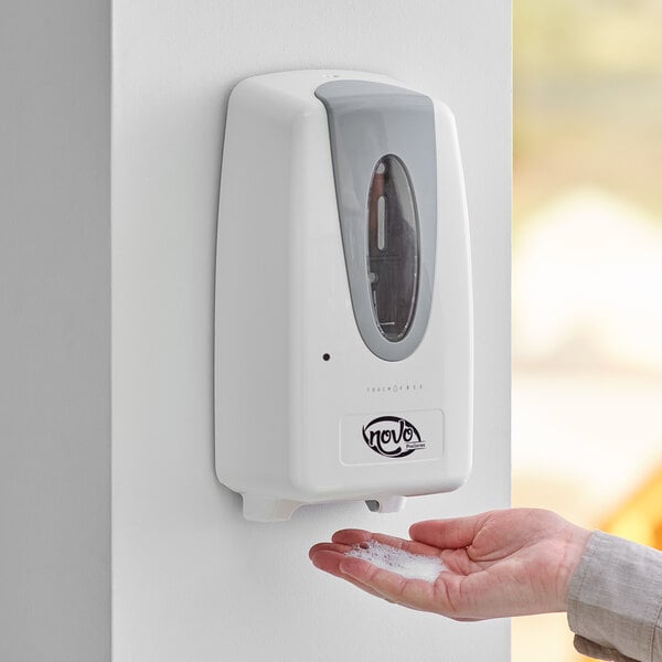 A person's hand using a white Noble Chemical touch-free hand sanitizer dispenser.