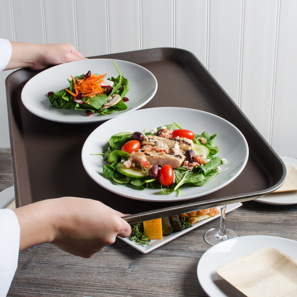 A person holding a Cambro non-skid serving tray with a plate of salad with carrots and mushrooms.