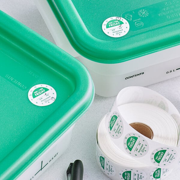 A roll of white Noble Products day of the week labels with green and white labels on two green containers.