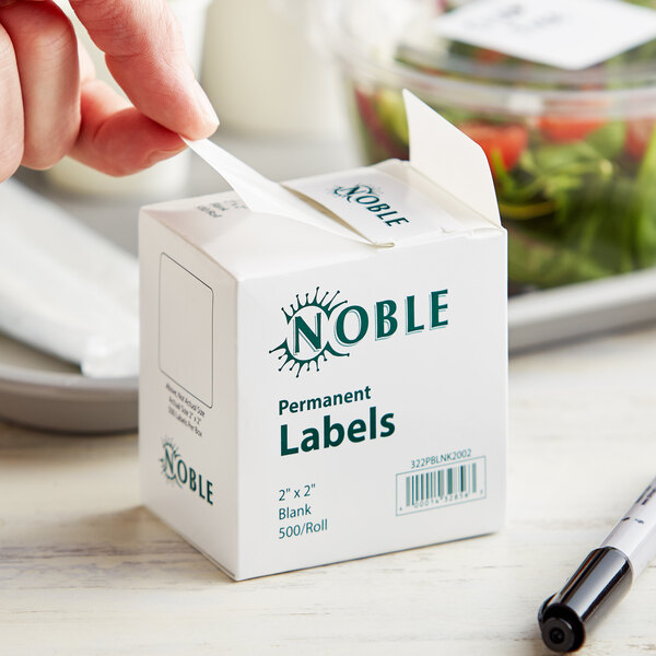 A hand putting a Noble 2" x 2" permanent blank label on a food container.