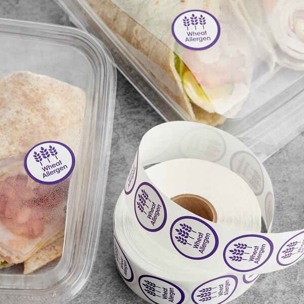 A roll of Point Plus wheat allergen labeling stickers on a table with two containers of food.