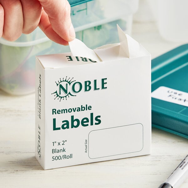 A hand putting a white Noble Products box of removable labels on a table.