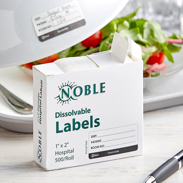 A white box of Noble Products dissolvable labels with green text on a table next to a salad.