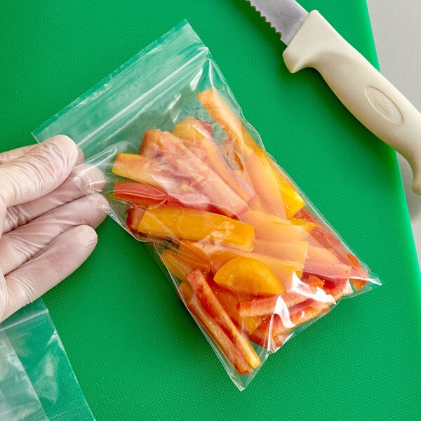 A hand using a knife to cut carrots in a Clear Line plastic food bag.
