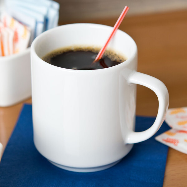 A stackable white porcelain mug filled with coffee with a straw in it.