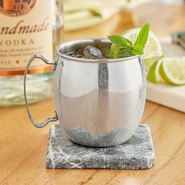 An Acopa silver Moscow Mule mug with ice and mint leaves on a marble table.
