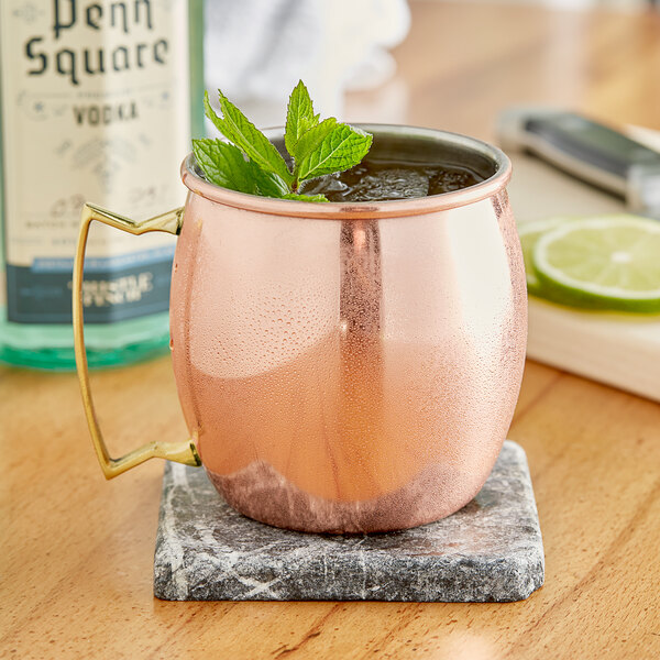An Acopa Alchemy copper Moscow Mule mug filled with a leafy drink on a counter.