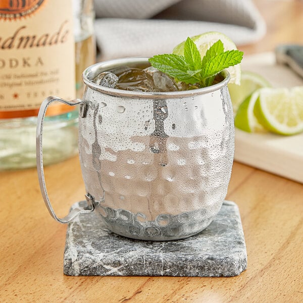 An Acopa silver Moscow Mule mug filled with ice and mint leaves on a marble counter.