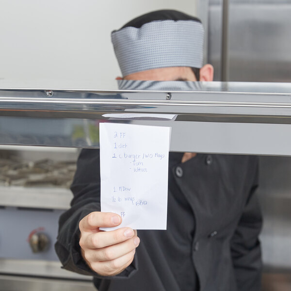 A chef using a Thunder Group stainless steel ticket holder to display a white paper with blue writing.