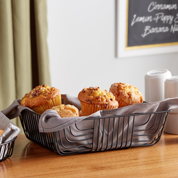 A rectangular black metal wire basket filled with muffins on a bakery counter.