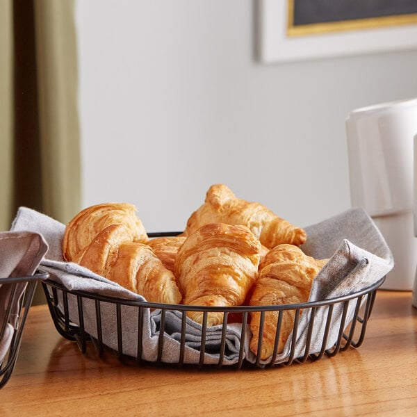 A round black wire basket filled with croissants on a table.