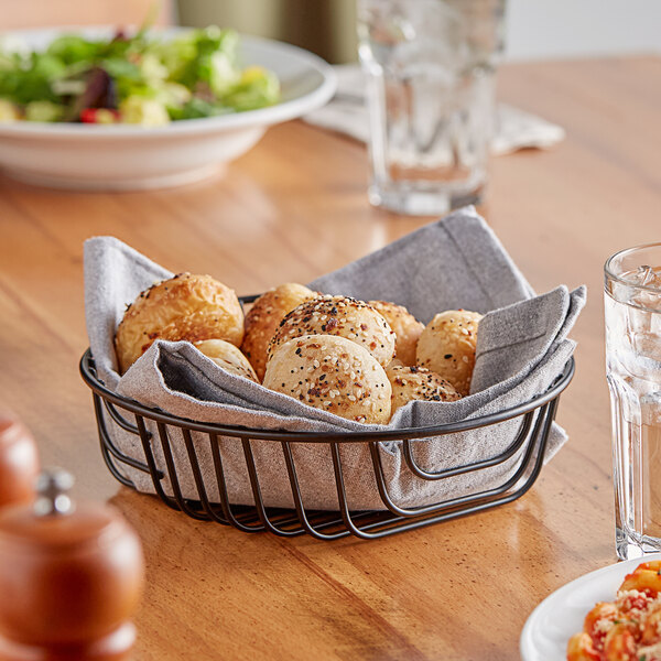 An Acopa round black wire basket filled with bread on a table.