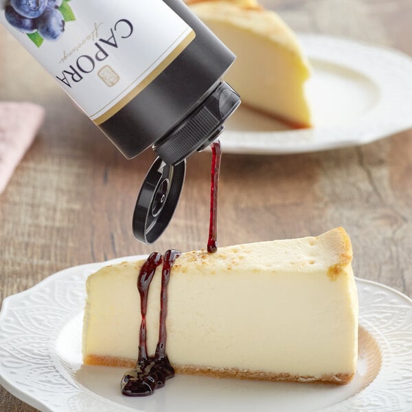 A bottle of Capora Blueberry Flavoring Sauce on a table with a cheesecake.