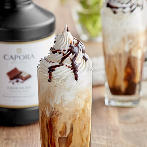 A glass of liquid with whipped cream and Capora Chocolate Flavoring Sauce.