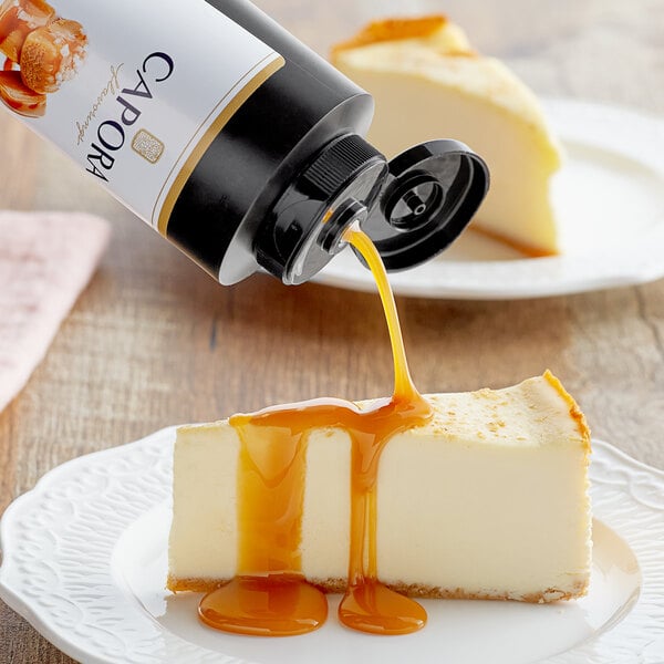 A Capora bottle pouring Salted Caramel Flavoring Sauce onto a slice of cheesecake.