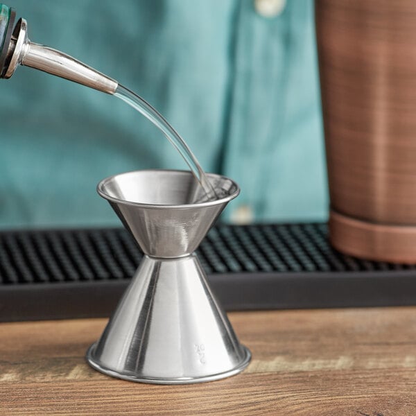 A person using an Acopa stainless steel classic jigger to pour a drink.