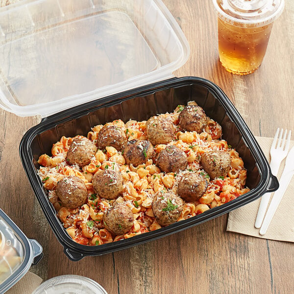 A black plastic Choice container with pasta and meatballs on a table.