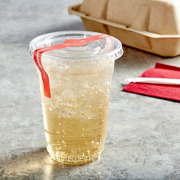 A clear PET plastic cup with a drink in it and a flat lid with a straw and tamper evident label.
