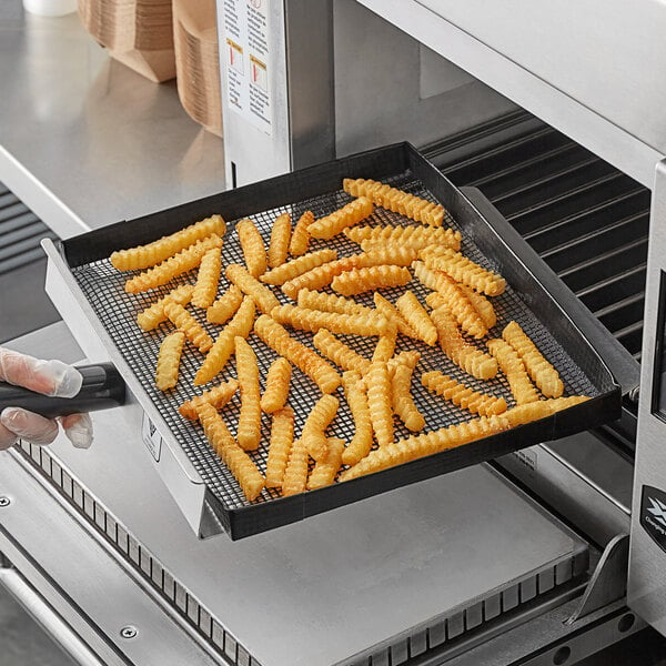 A person holding a Baker's Mark mesh basket of french fries in front of a black oven.