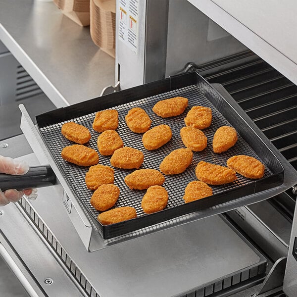 A person using a Baker's Mark loose weave mesh basket to cook chicken nuggets in a rapid cook oven.