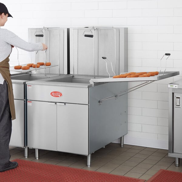 A man using an Avantco natural gas flat bottom fryer to cook donuts.