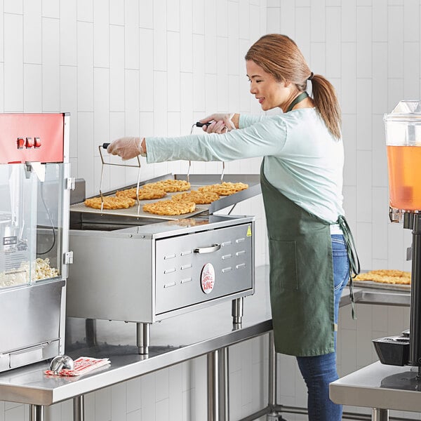 A woman using a Carnival King countertop funnel cake and donut fryer in a commercial kitchen.