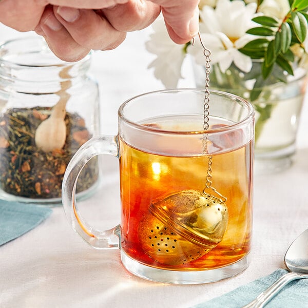 A Fox Run tea ball infuser with chain in a glass mug of tea.