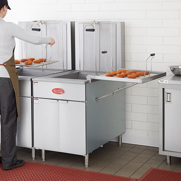 A man wearing an apron cooking donuts in an Avantco natural gas fryer.