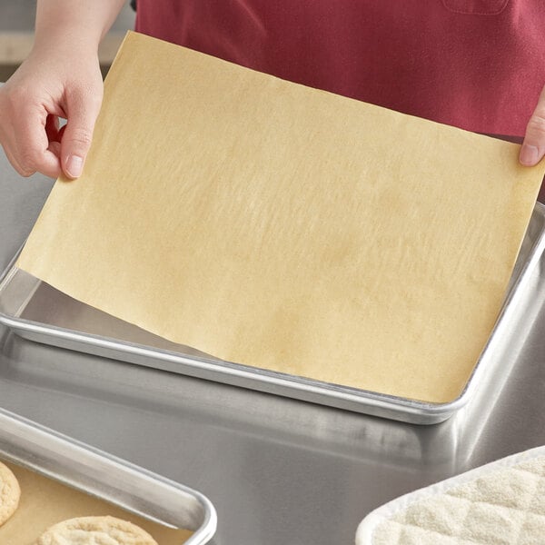 A person placing a Baker's Mark unbleached quilon-coated parchment paper sheet on a baking tray.