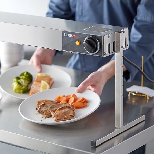 A person using a ServIt strip warmer to serve a plate of meat and carrots on a table.