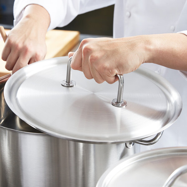 A person using a Vollrath stainless steel lid to cover a pot.