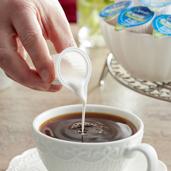 A person pouring Splenda French Vanilla creamer into a cup of coffee.