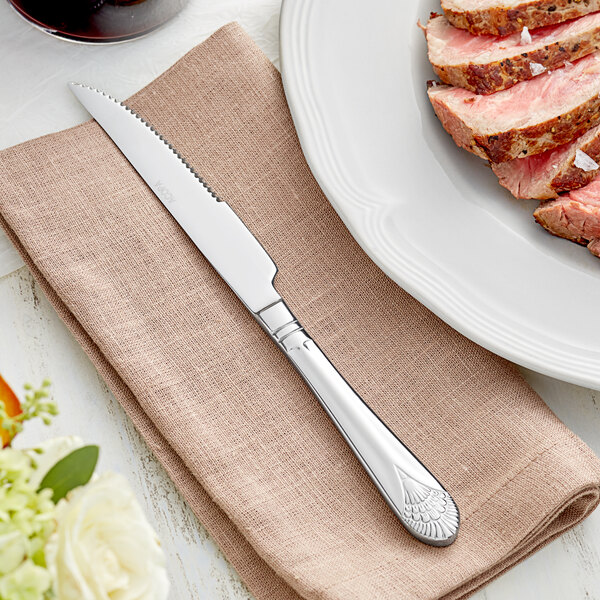 An Acopa Monaca steak knife on a napkin next to a plate of meat.