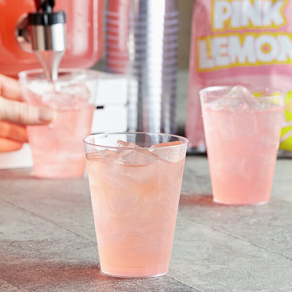 A hand holding a clear plastic cup of pink DominAde.