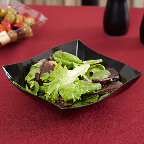 A bowl of salad in a black Fineline Wavetrends serving bowl on a red table.
