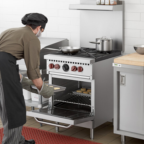 A man in a black chef's hat and apron using a Vulcan commercial gas range to put food into an oven.