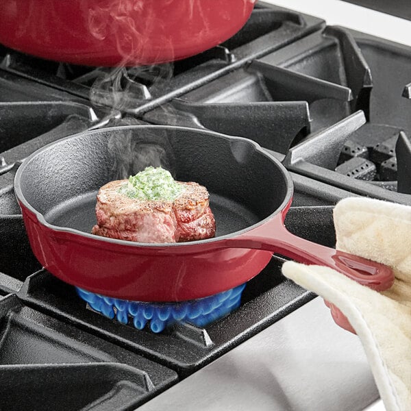 A person cooking a piece of meat in a Valor merlot enameled cast iron skillet.