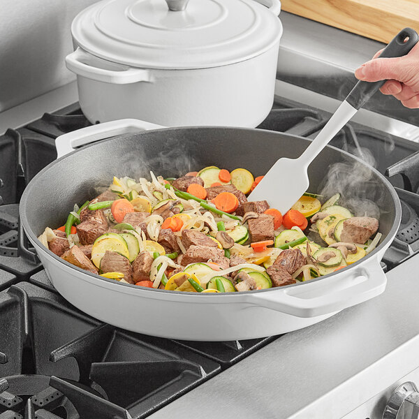 A person cooking meat and vegetables in a Valor Arctic White enameled cast iron skillet.