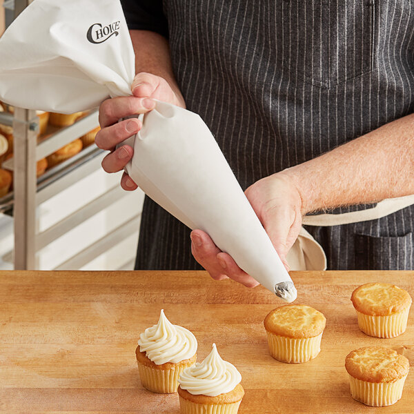 A person using a Choice white plastic coated canvas pastry bag to frost cupcakes.