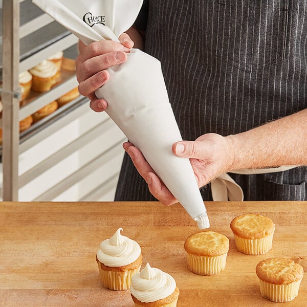 A person using a Choice Plastic Coated Canvas Pastry Bag to pipe white frosting onto cupcakes.