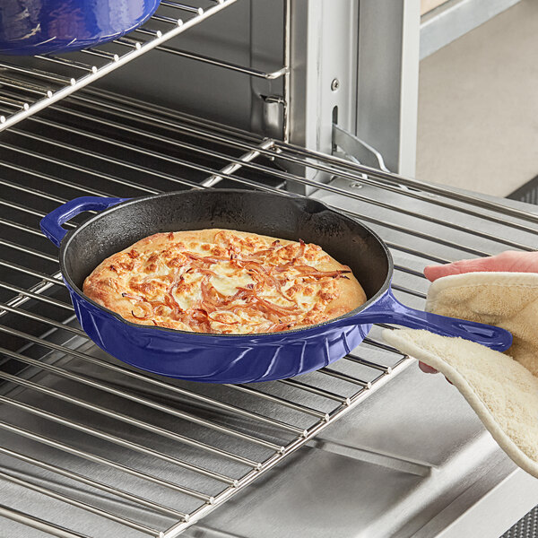 A person using a Valor Galaxy Blue enameled cast iron skillet to cook a pizza.