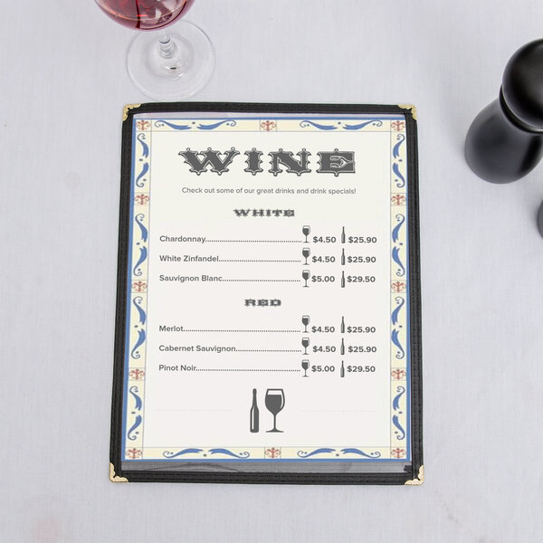 A menu with a Mediterranean border on a counter with a glass of wine.